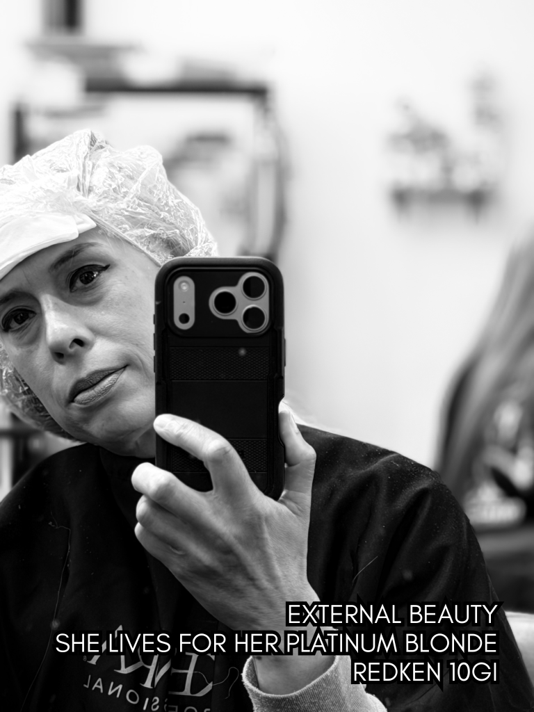 Black-and-white mirror selfie of Baroque Medusa during a hair appointment, paired with a haiku about beauty, artifice, and self-construction.