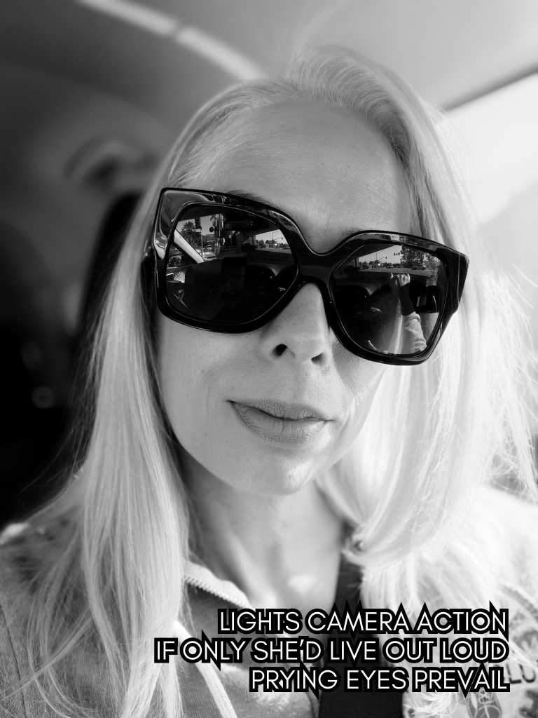 Black-and-white selfie of Baroque Medusa wearing sunglasses in a car, paired with a haiku about visibility, performance, and surveillance.