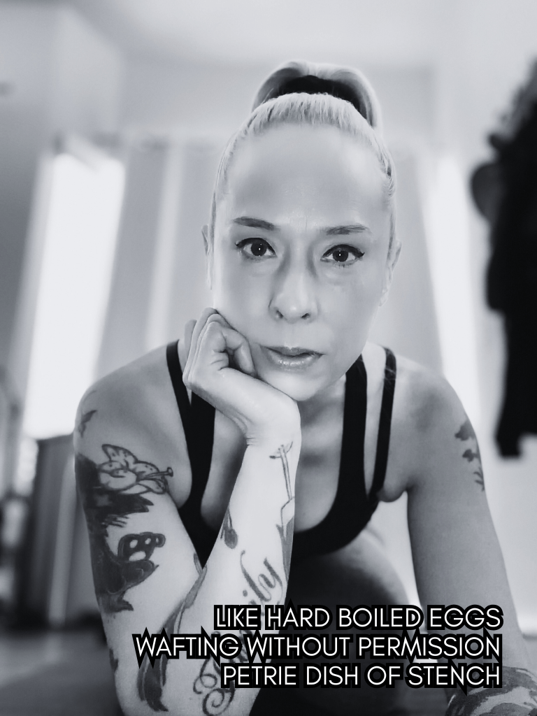 Black and white self-portrait of Baroque Medusa resting her chin on her hand with visible arm tattoos, overlaid with a haiku about hard boiled eggs and decay.