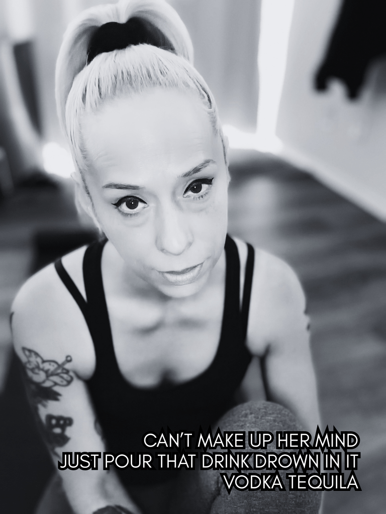 Black and white portrait of Baroque Medusa seated on the floor, looking up at the camera, overlaid with a haiku referencing indecision and alcohol.