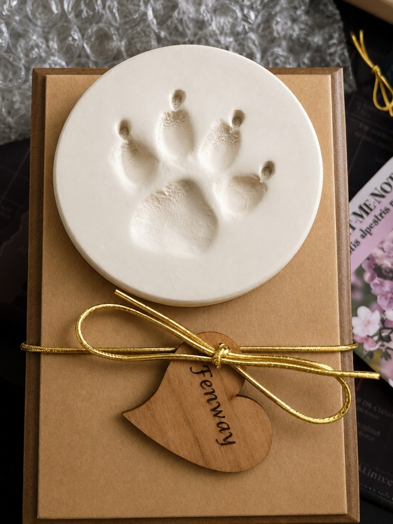 Fenway’s memorial paw print displayed beside a wooden heart tag engraved with her name after her passing.